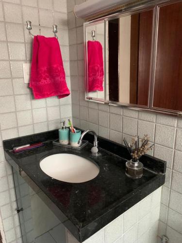 La salle de bains est pourvue d'un lavabo, d'un miroir et de serviettes rouges. dans l'établissement Apartamento bancários, à João Pessoa