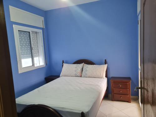 Dormitorio azul con cama y ventana en appart hotel tanger gzenaya, en Tánger