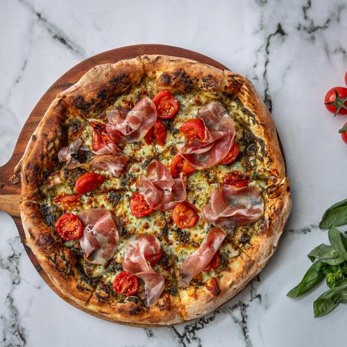 a pizza with tomatoes and ham on a table at Native Rose Hotel in Sydney