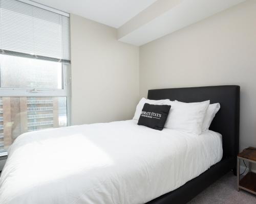 a white bed with a black headboard and a window at Hendrix Luxury Apartments by Corporate Stays in Edmonton