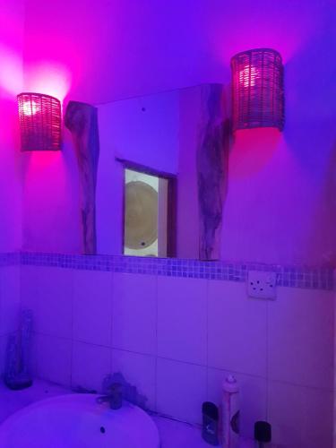 a bathroom with purple lighting and a sink and a mirror at Edenic in Diani Beach