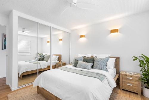 a white bedroom with two beds and a mirror at Maroochydore Beachfront in Maroochydore