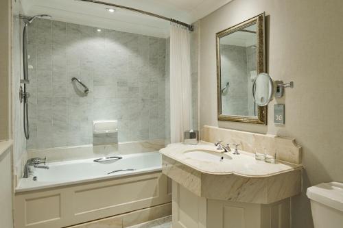 a bathroom with a sink and a tub and a mirror at Hanbury Manor Marriott Hotel & Country Club in Ware