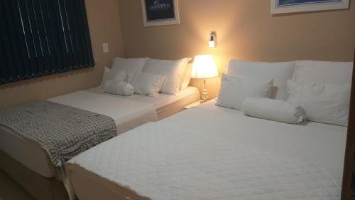 a bedroom with two beds with white sheets and a lamp at Casa 3 Encanto dos Mares in Barra Velha