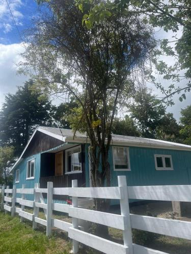 uma pequena casa azul atrás de uma cerca branca em Cabaña EL VIEJO SAM em Curaco de Velez