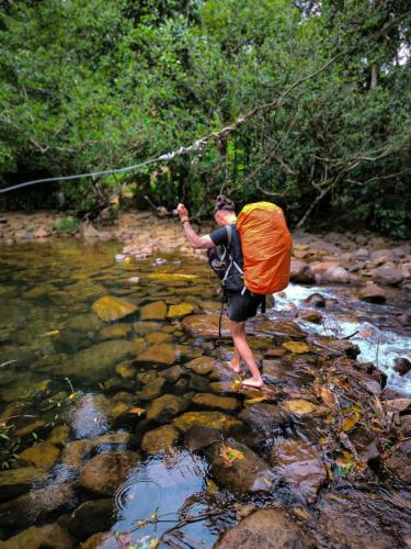 a person standing in a stream with a bag at Rainforest cabin in Deniyaya