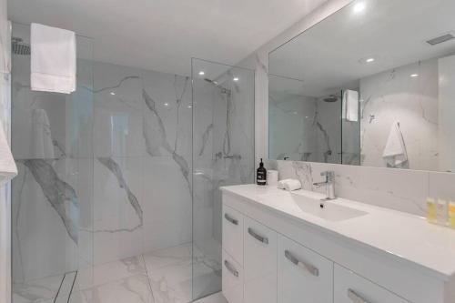 a white bathroom with a sink and a shower at Unit 15 @ Tropical Reef: 2 mins to Four Mile Beach in Port Douglas