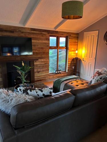 a living room with a leather couch and a television at Woodside Lodge, Weybourne, Holt in Weybourne