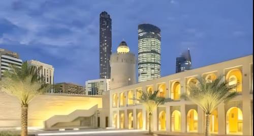 a building with palm trees in front of a city at Heart of Abu Dhabi - New Community Elite Room in Abu Dhabi