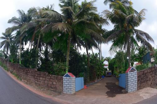 a retaining wall with palm trees and a road at Runnin Airport - Homestay in Gurpur