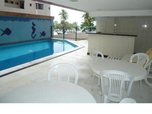 una piscina con mesas y sillas blancas junto a una mesa y una piscina en Flat em Recife, en Recife