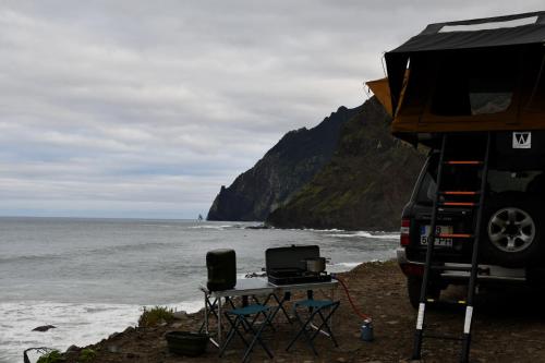 a camper with a grill and a table and chairs next to the ocean at Overland Madeira in Santana