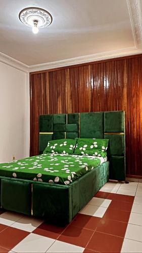 a green bed in a room with a wooden wall at Peaceful home in Yaoundé