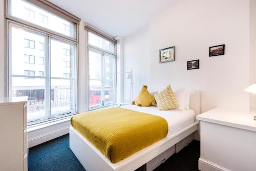 a bedroom with a bed with yellow sheets and windows at Apartments are located in the Heart of Shoreditch in London