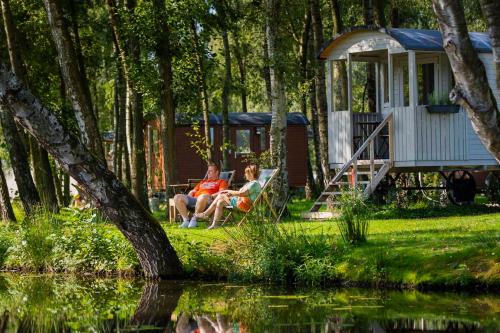 a man and woman sitting on a bench near a cabin at Glamping - 25 min Roermond, Maasmechelen & Maastricht in Kinrooi