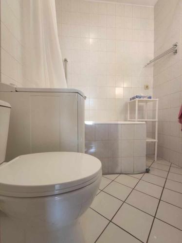 a white bathroom with a toilet and a tiled floor at Cosy Room in Pātan