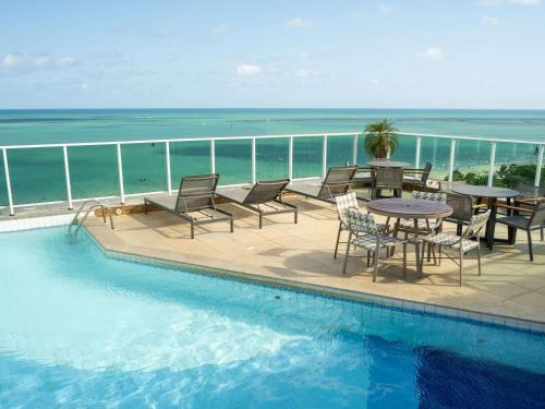 a swimming pool with a table and chairs and the ocean at Mercure Maceio Pajuçara in Maceió
