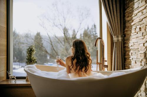 a woman sitting in a bath tub holding a glass of wine at Luxury Chalet Kajmer in Jurgów