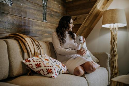 a pregnant woman sitting on a couch holding a cup of coffee at Luxury Chalet Kajmer in Jurgów