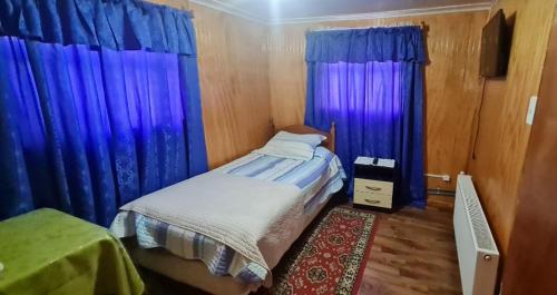 een slaapkamer met blauwe gordijnen en een bed met een tapijt bij Hostal Beagle in Puerto Williams