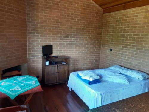 sypialnia z łóżkiem, telewizorem i stołem w obiekcie Chalé Recanto Lobo Guará w mieście Gonçalves