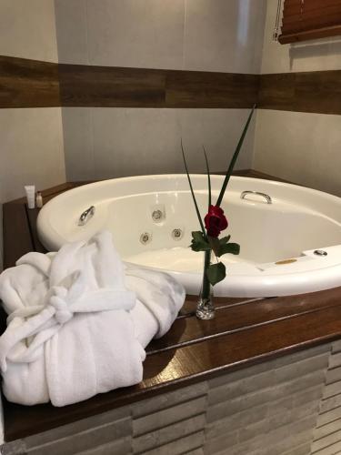 a bath tub with towels and a vase with a rose at Pousada Déllis in Visconde De Maua