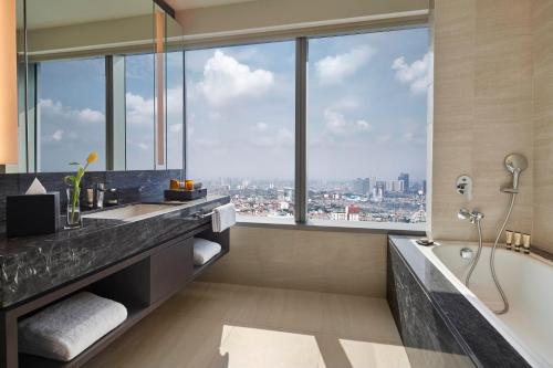 La salle de bains est pourvue d'une baignoire et d'une grande fenêtre. dans l'établissement PARKROYAL Serviced Suites Jakarta, à Jakarta