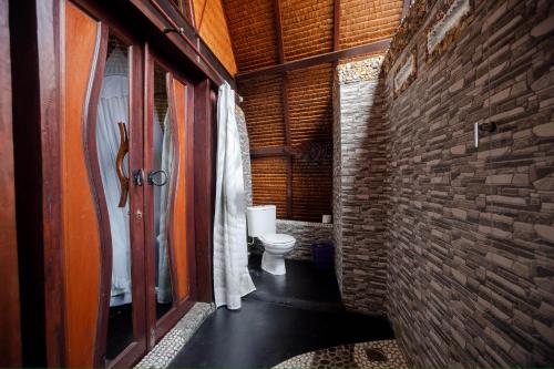 a bathroom with a toilet and a brick wall at Green Travelodge Bukit Lawang in Bukit Lawang