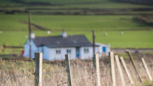 a fence with a blue house in the middle of a field at Ty Cwyfan in Aberffraw