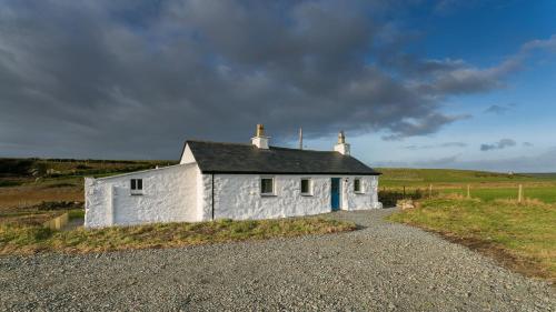 a small white building on the side of a gravel road at Ty Cwyfan in Aberffraw
