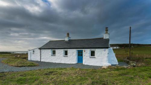 a white house with a blue door in a field at Ty Cwyfan in Aberffraw