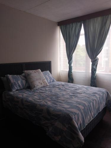 Schlafzimmer mit einem Bett und einem Fenster mit Vorhängen in der Unterkunft Comfy spacious apartment in Pretoria