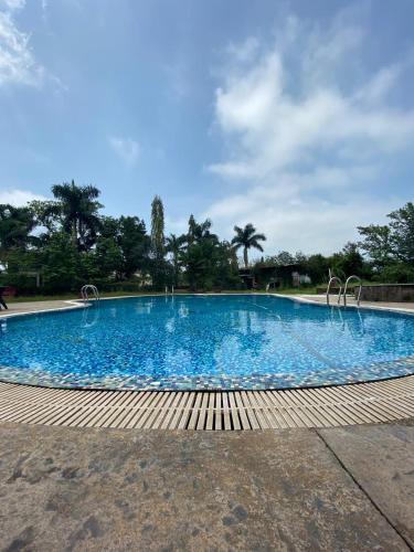 a large blue swimming pool with trees in the background at Dukes Den Resort in Lonavala