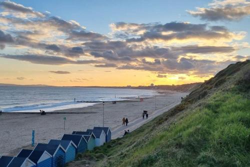 a beach with blue beach huts and a sunset at Cosy Bournemouth Bungalow in Longham