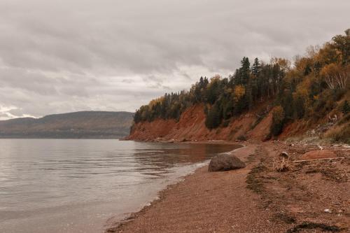 a shore of a body of water with trees and mountains at Chalet La Renarde in Nouvelle