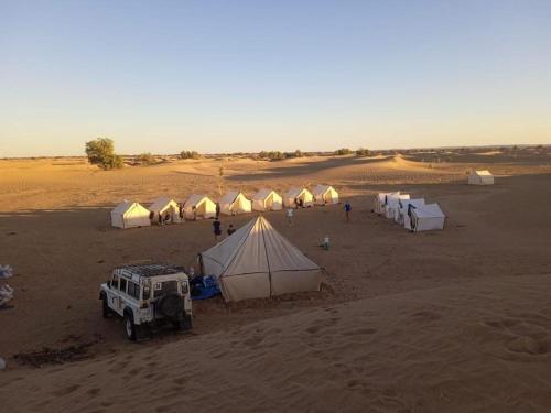 a group of tents and a jeep in a desert at Itri camp in Zagora