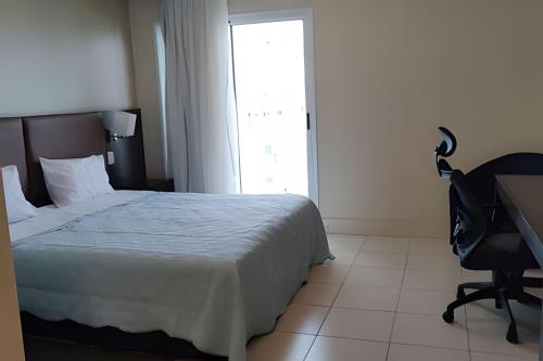 a bedroom with a bed and a desk and a window at Studio pé na areia, vista, internet e ar in Macaé