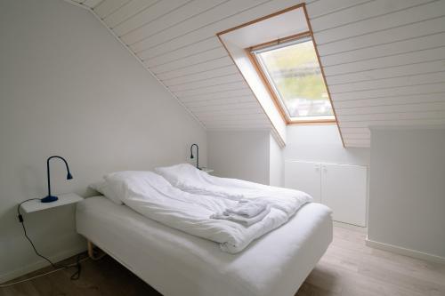 a bedroom with a bed with white sheets and a window at Spacious City Center Home by the Sea in Klaksvík