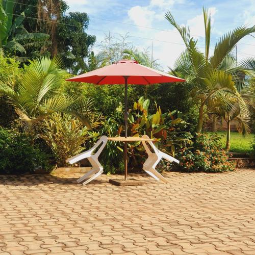 Ambur Gardens Nalya في كامبالا: مظلة حمراء وكرسي تحت طاولة