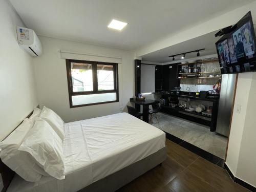 1 dormitorio con 1 cama blanca y TV en Quitinete Em Bombinhas, en Bombinhas