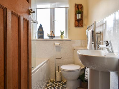 baño con lavabo y aseo y ventana en Pike Cottage, en Hinderwell