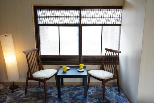 dos sillas y una mesa con dos tazas delante de una ventana en 桜香楽　宮津町家　Sakara Miyazu-Machiya en Miyazu