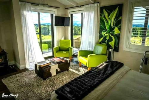 a bedroom with a bed and two green chairs at Quail Run Cottage with stunning vineyard views in Renwick