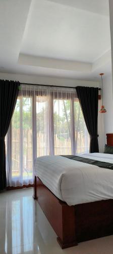 a bedroom with a large bed in front of windows at ZiFa Mandalika in Kuta Lombok
