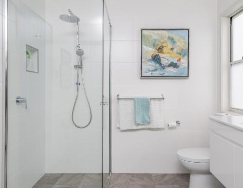 a white bathroom with a shower and a toilet at 'South Pacific' - Luxury Oceanfront at Culburra! in Culburra Beach