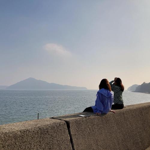 three women sitting on a wall looking at the water at Private Chill Base たまて 三豊市荘内半島の古民家宿 一棟貸しも可 in Mitoyo