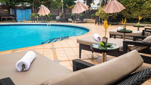 a swimming pool with tables and chairs next to a resort at Oak Plaza Hotels East Airport in Accra
