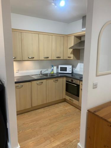 cocina con armarios de madera, fregadero y microondas en Aspect apartments en Chesham