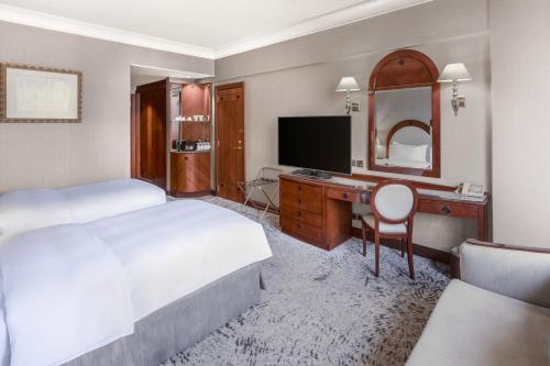 a hotel room with two beds and a desk with a television at Madinah Hilton Hotel in Al Madinah