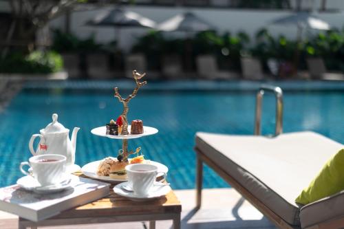 a tray of food and coffee cups on a table by a pool at Woodlands Suites Serviced Residences - SHA Extra Plus in Pattaya North